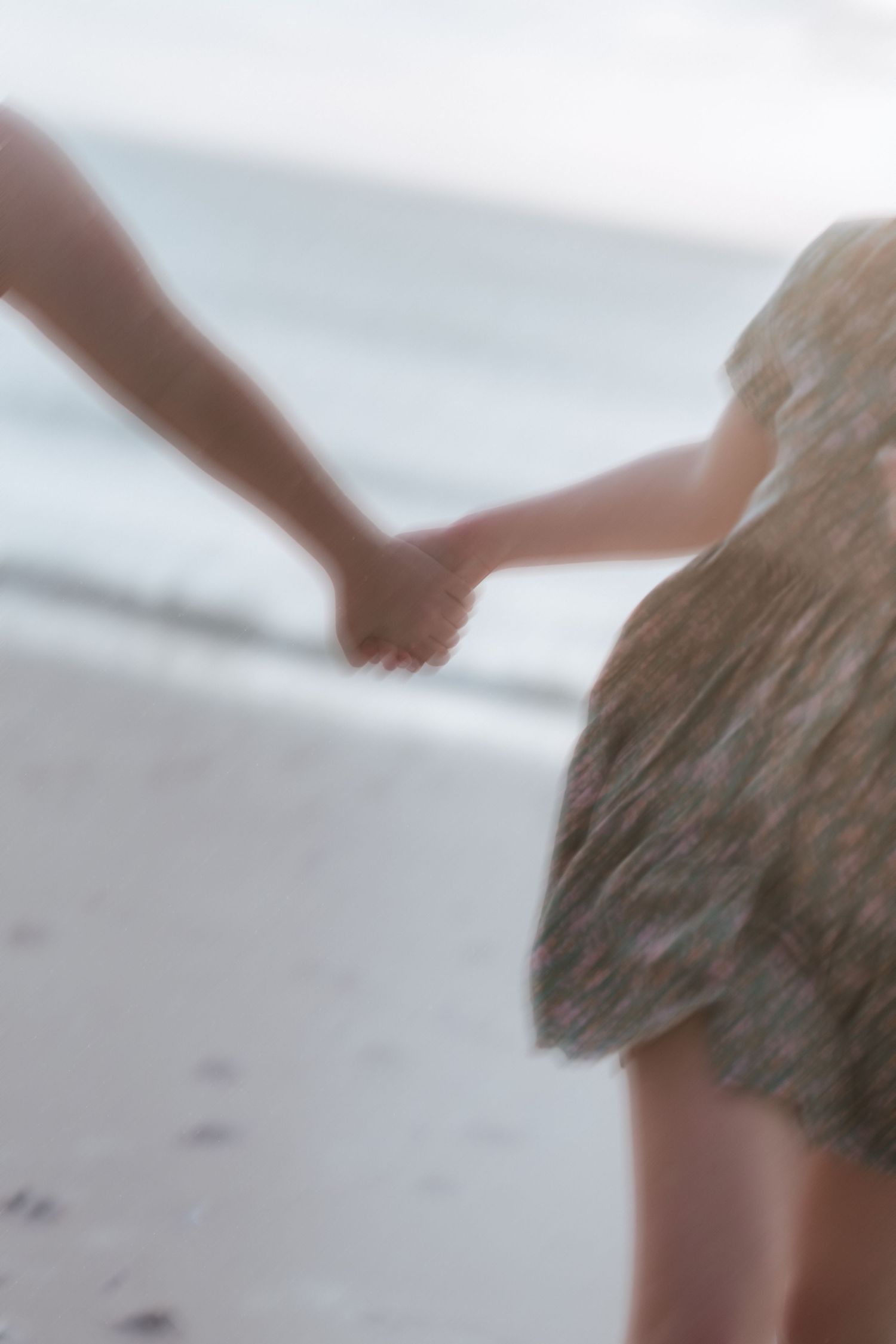 Close-up view of holding hands against a soft blurred beach background with flowing dress fabric.