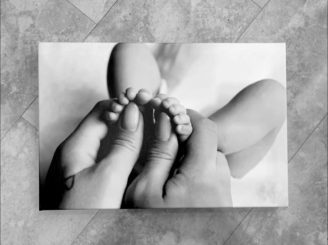 A close-up black and white photo shows tiny baby feet being gently held by adult hands in a tender moment.