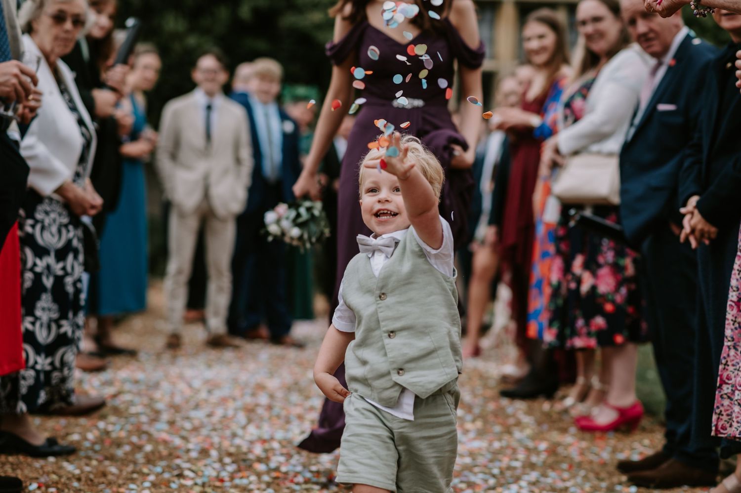 A young child running with confetti in his hands, throwing it joyfully at the bride and groom.