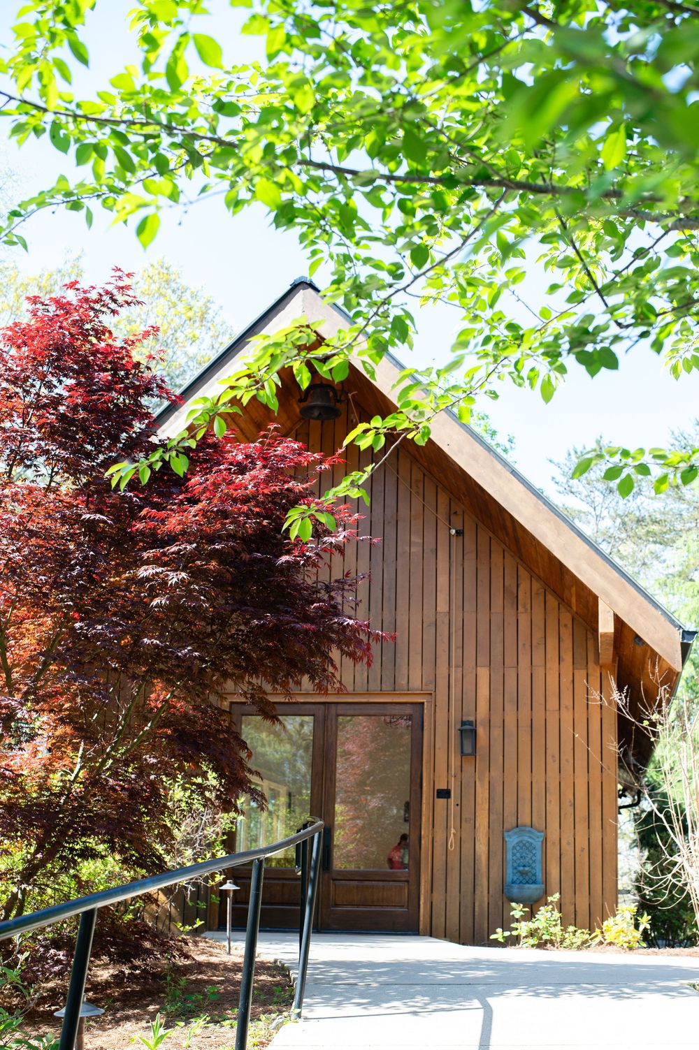 Modern wooden cabin with dark brown vertical siding and angled roof nestled among red maple and green trees. Juliette Chapel Wedding photos
