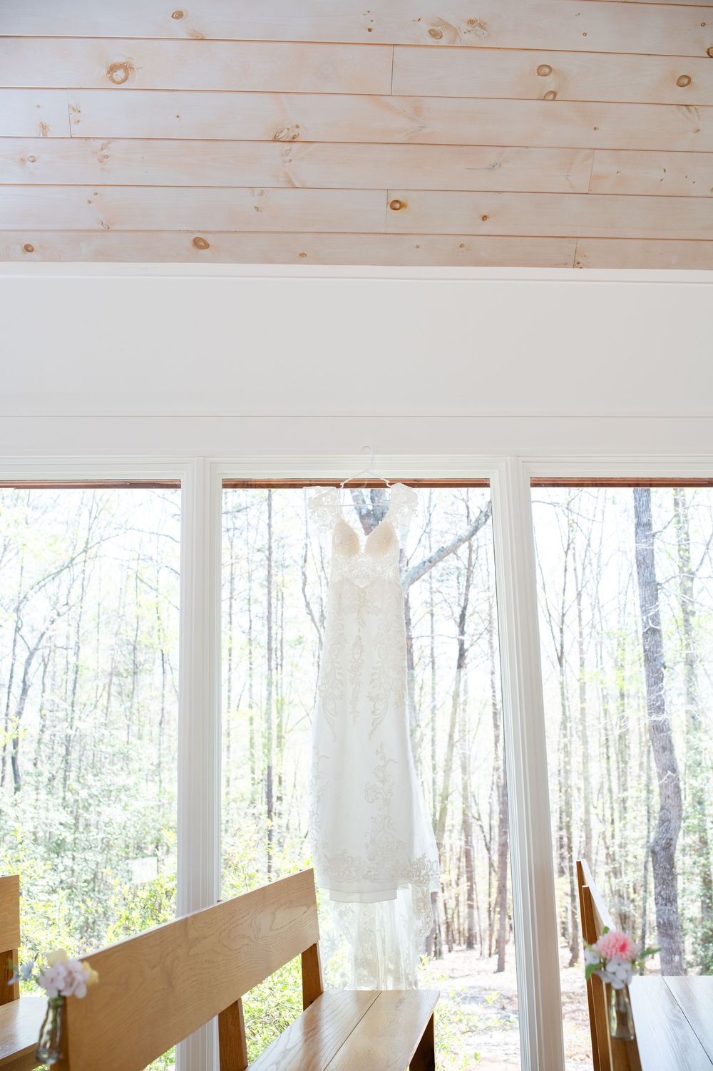 White wedding dress hanging in a rustic wooden cabin with large windows overlooking a forest setting. Juliette Chapel Wedding photos