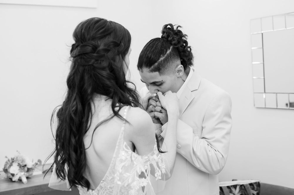A black and white wedding photograph showing an emotional moment between two brides in elegant wedding attire.