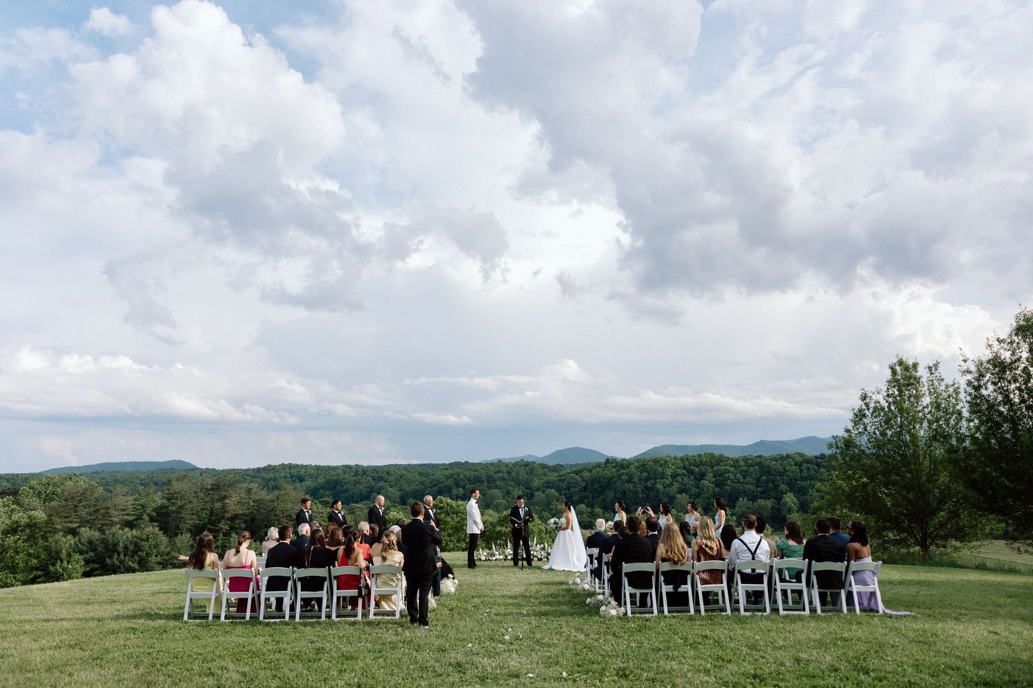 Outdoor wedding ceremony setup on a hilltop with white chairs and stunning mountain views in the distance.
