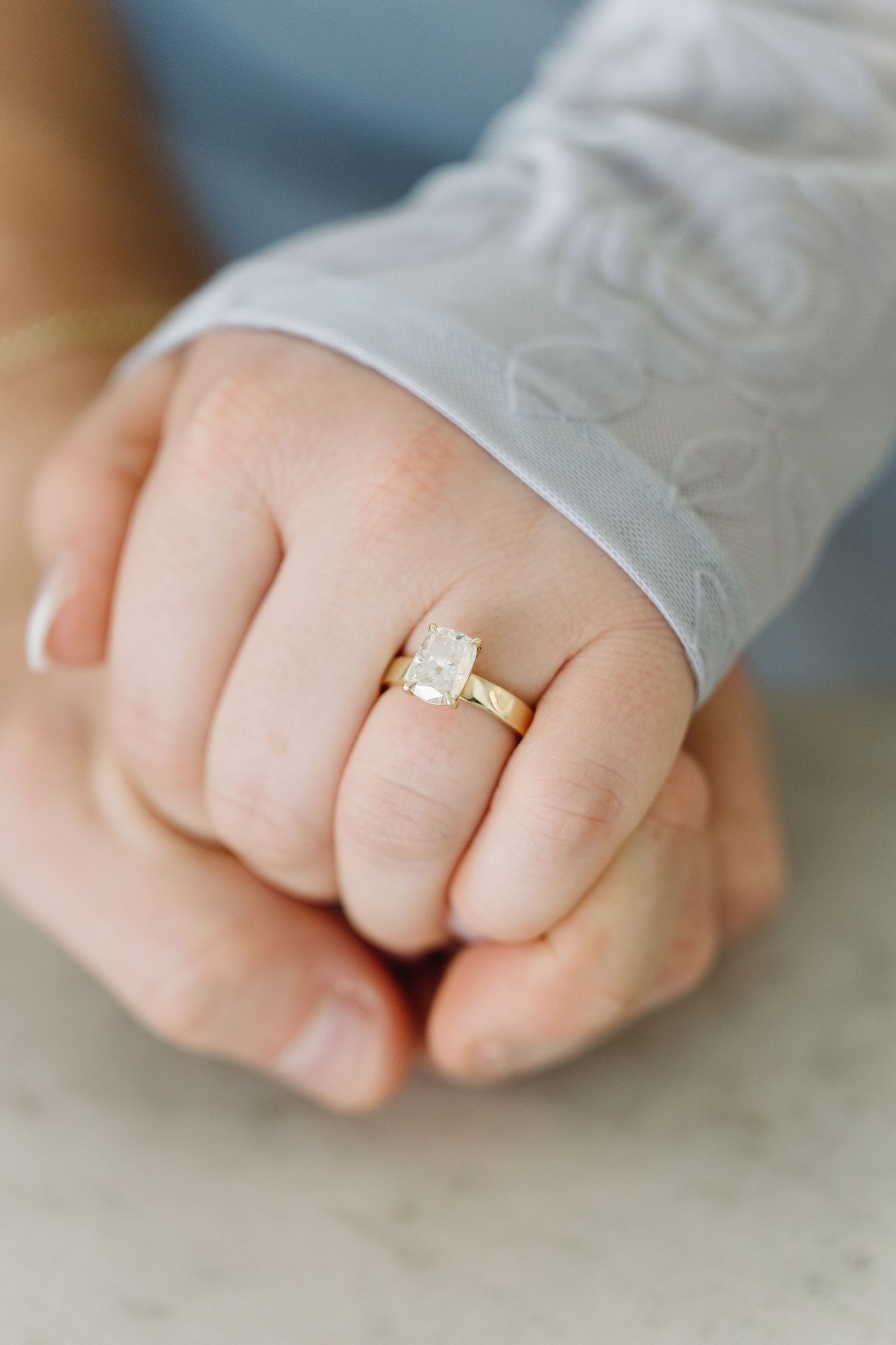 A delicate gold engagement ring with a rectangular raw crystal stone set on a simple band against a marble background.