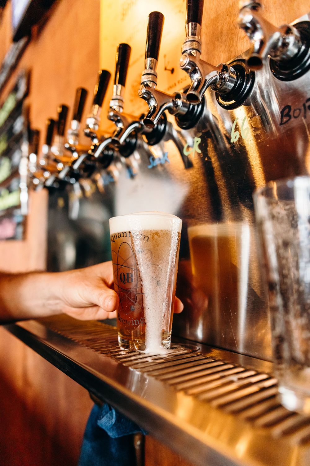 Multiple beer taps lined up at a wooden bar counter showing draft beer selection in warm amber lighting.