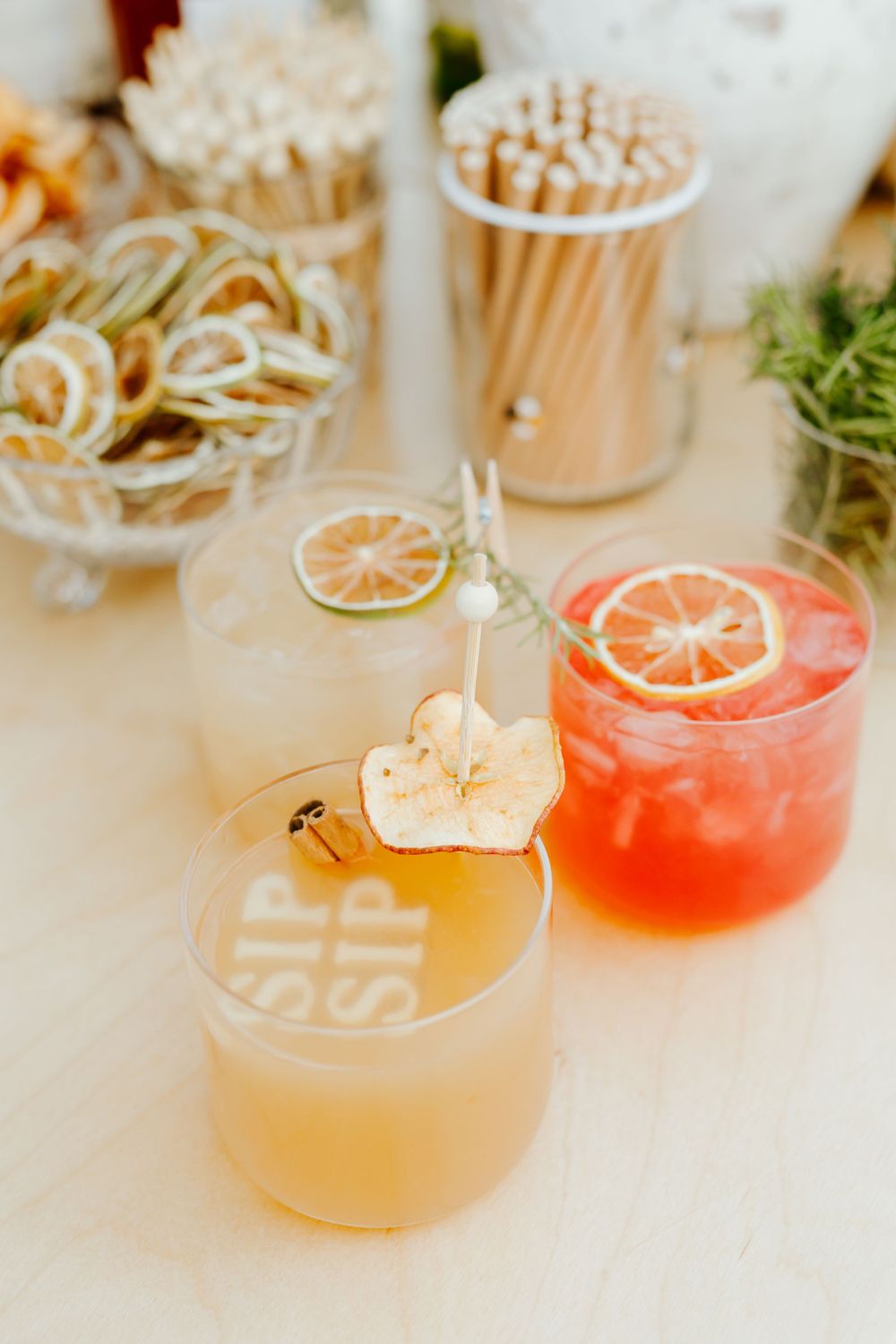 Two artisanal cocktails garnished with citrus and dried apple chips served at an elegant bar with room for straws and decor.