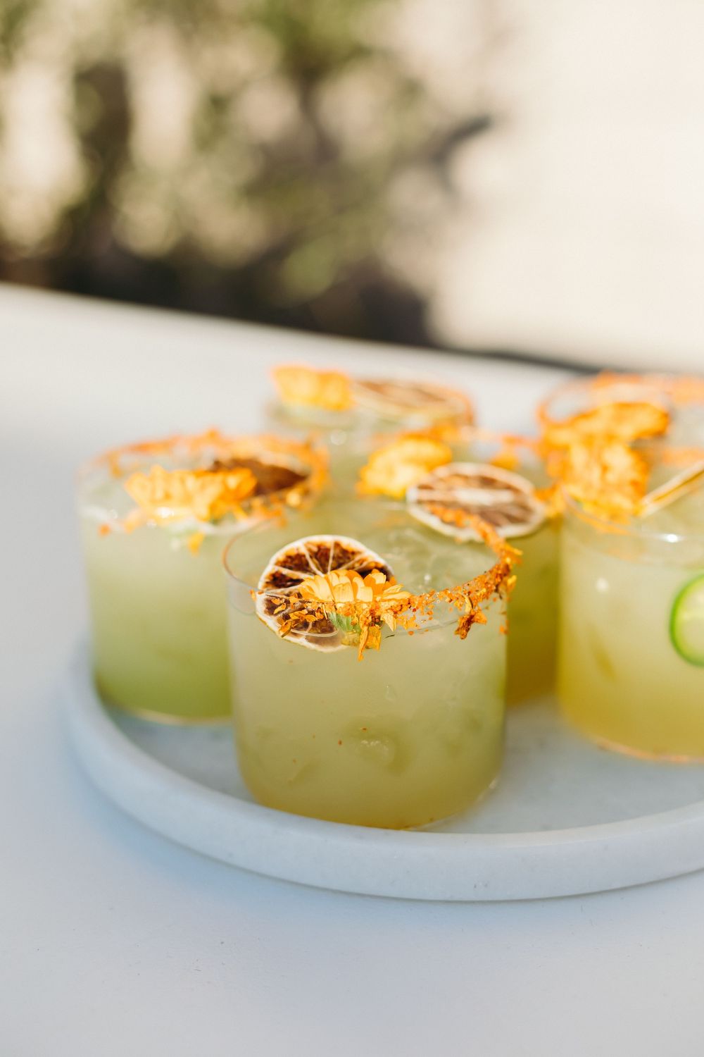 Refreshing citrus cocktails garnished with dried lime slices and glowing orange zest on a white marble plate.