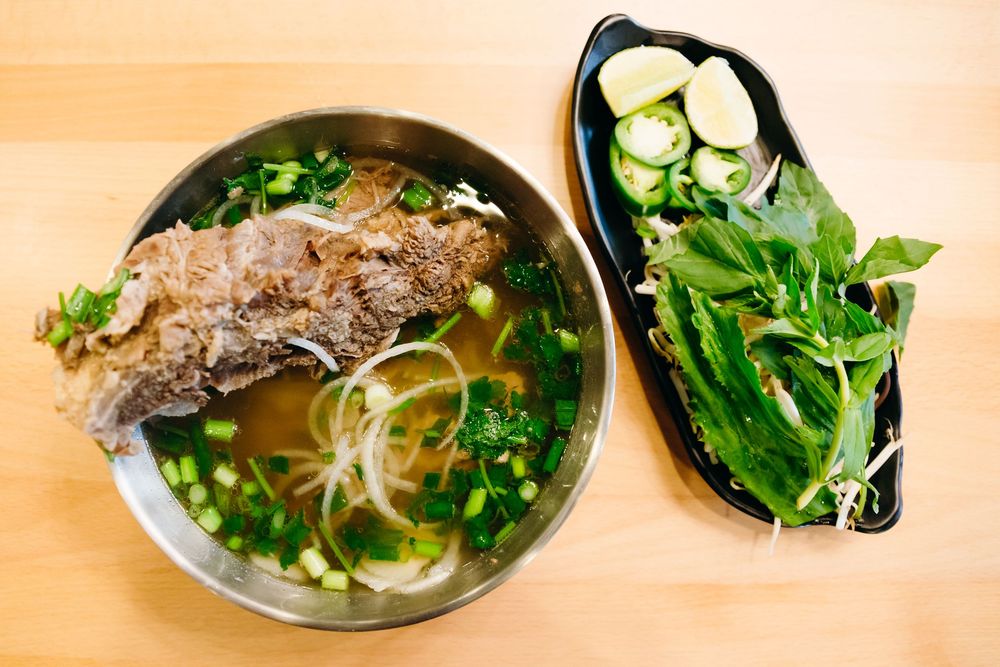 A row of Vietnamese pho noodle soup bowls filled with broth, herbs, meat, and fresh garnishes lined up on a counter.