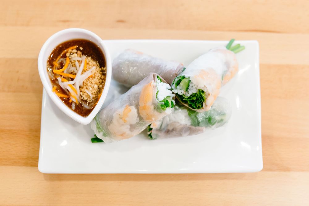 Fresh Vietnamese spring rolls with shrimp and vegetables lined up on a white rectangular plate.