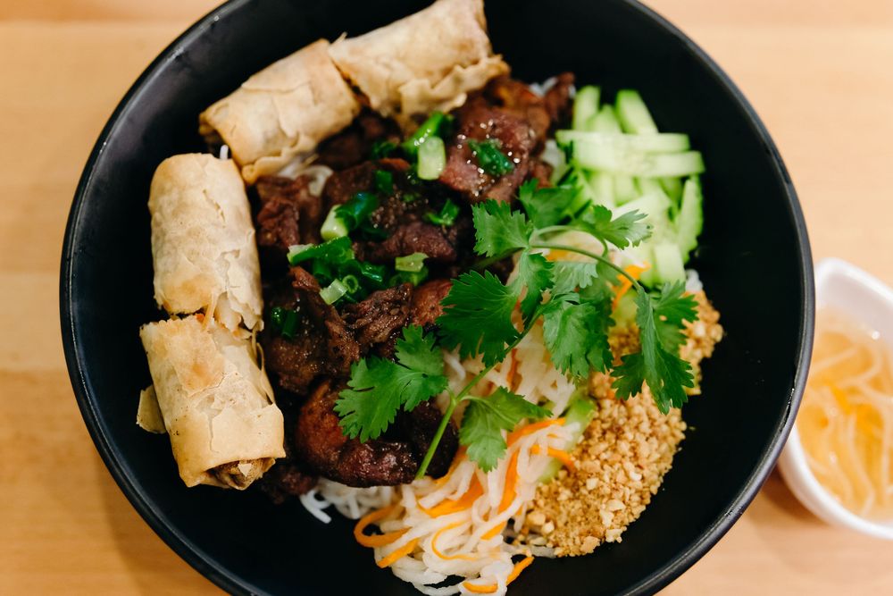 A Vietnamese bowl with spring rolls, grilled meat, vermicelli noodles, fresh herbs and crushed peanuts.
