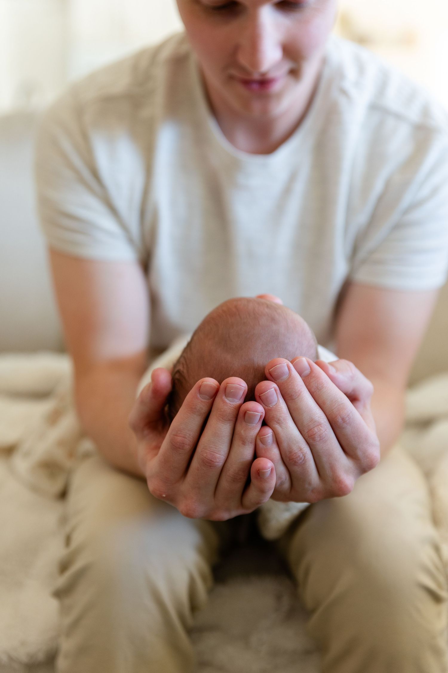 dad holding a newborns tiny head in his large hands.