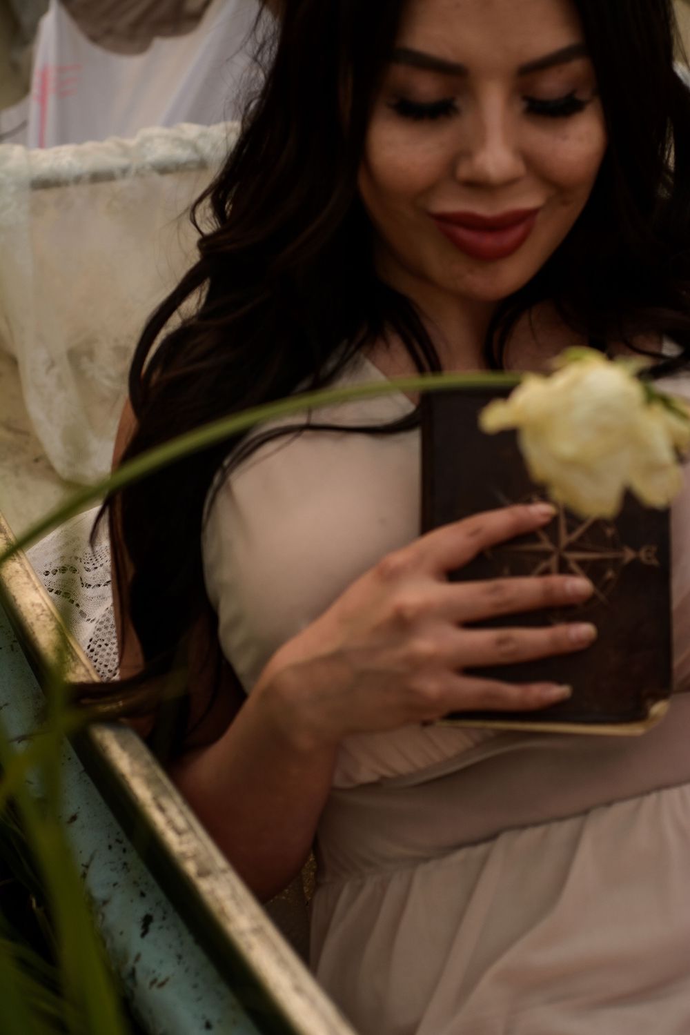 A delicate scene with white flowers and a vintage book, featuring an elegant cream dress and soft natural lighting.