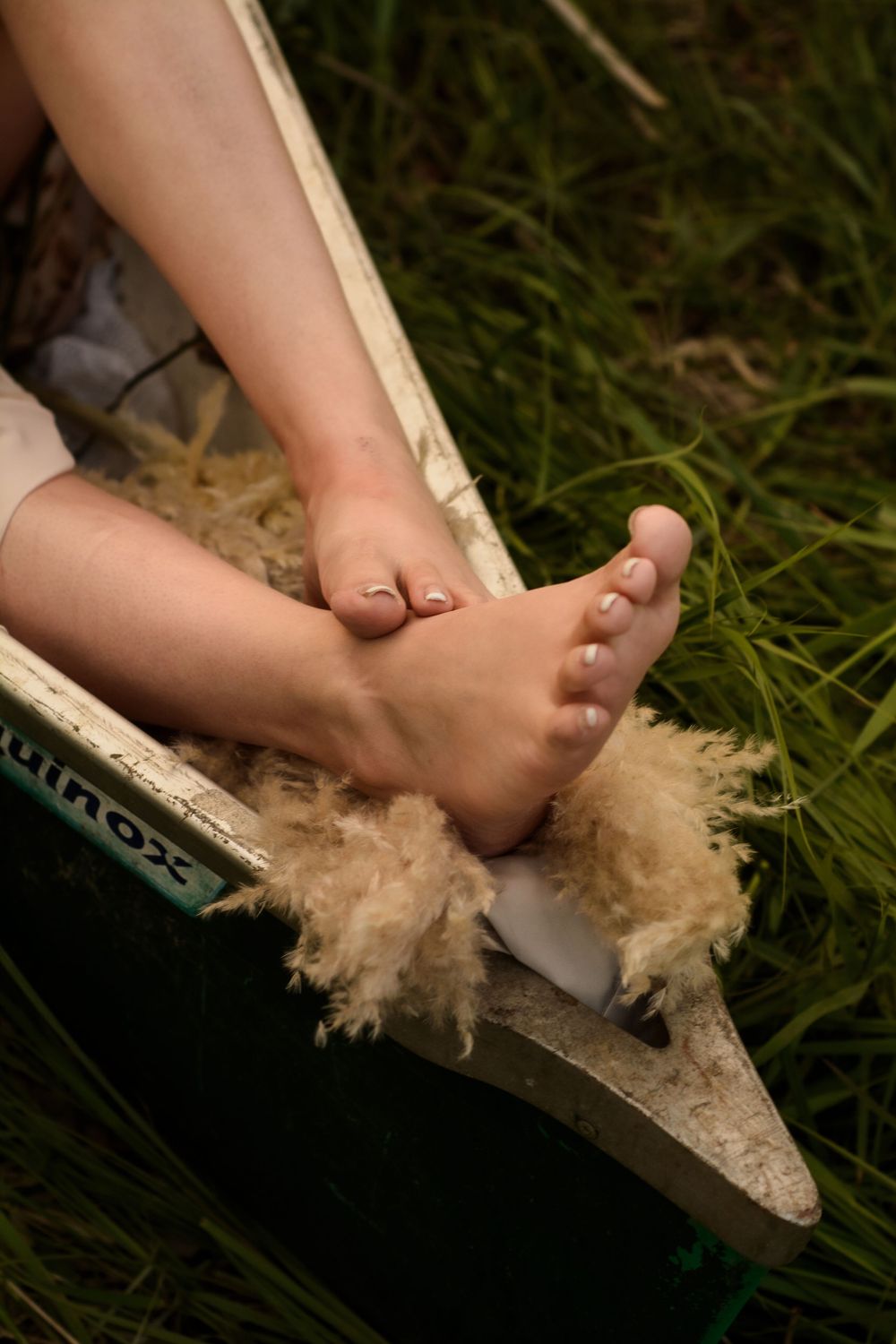 Bare feet resting on a furry sheepskin blanket in a canoe with tall grass in the background.