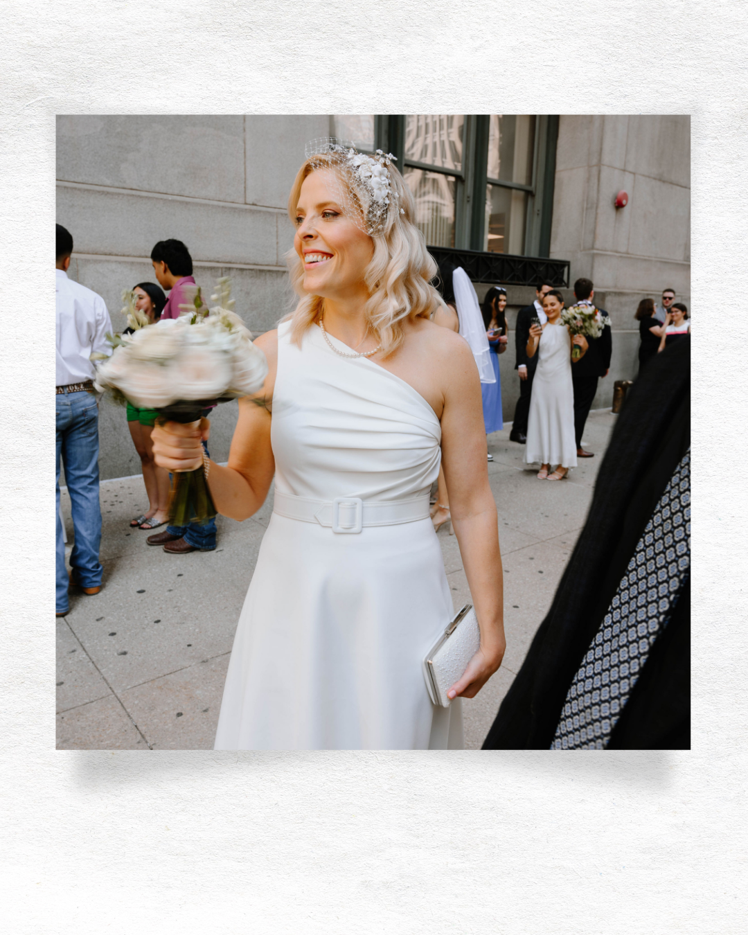 A bride in a white wedding dress strikes playful poses against a stone building exterior while celebrating.