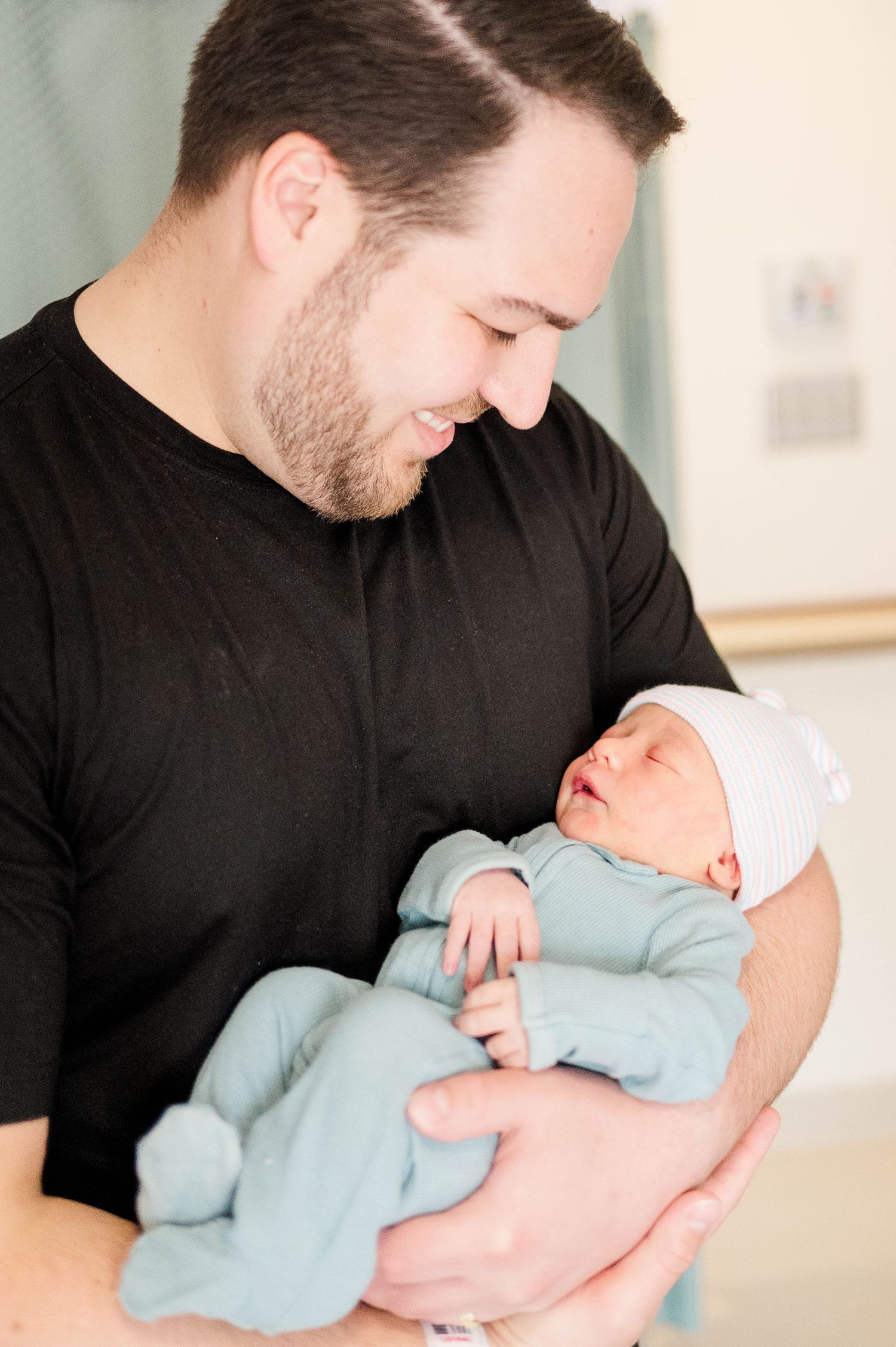 A tender moment in soft natural light shows a person in black holding a sleeping newborn baby in light blue.