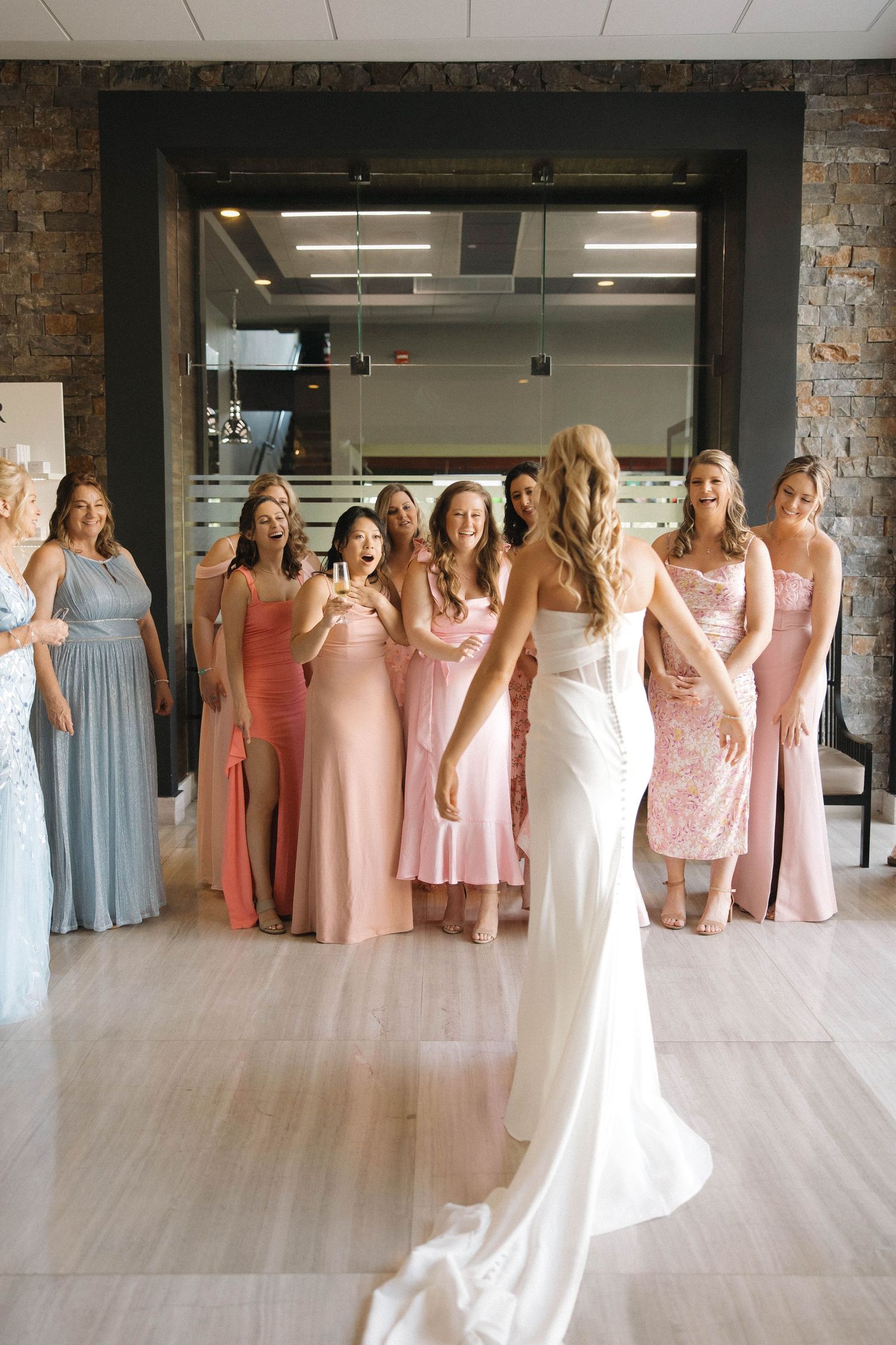 A bride in a sleek white dress with thigh slit gets help adjusting her gown in an elegant indoor setting.