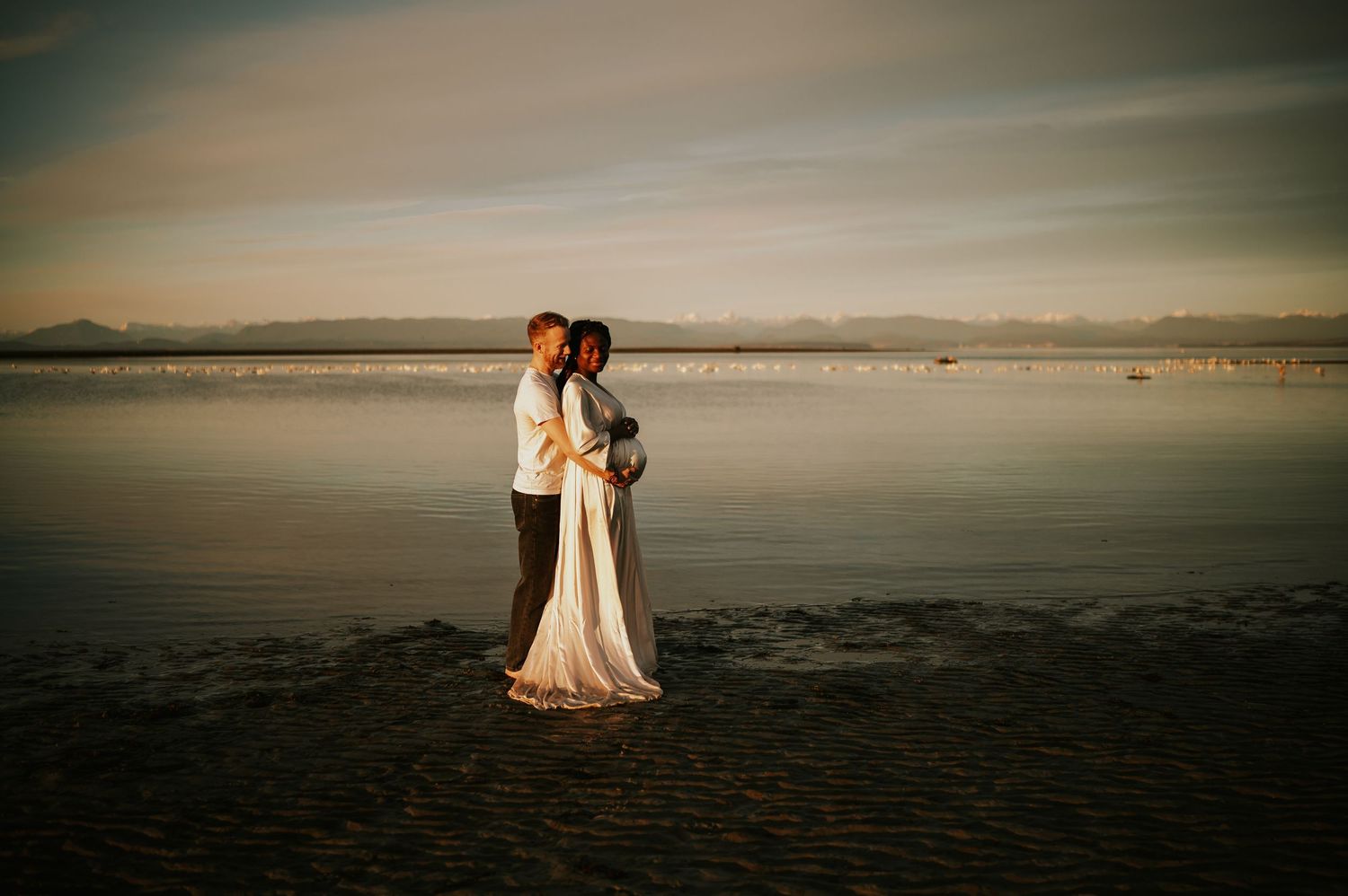Maternity portrait photography of couple holding bump at kye bay beach by ocean during sunset Comox Valley Vancouver Island photographer