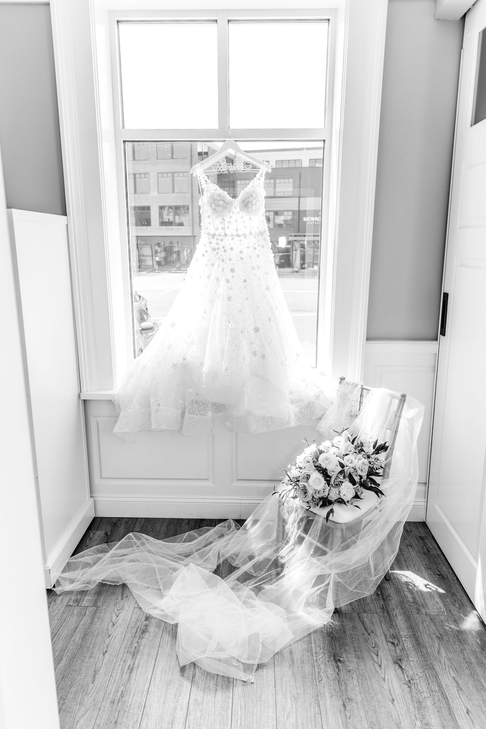 White wedding dresses hanging in a sunlit room with wooden floors and large windows.
