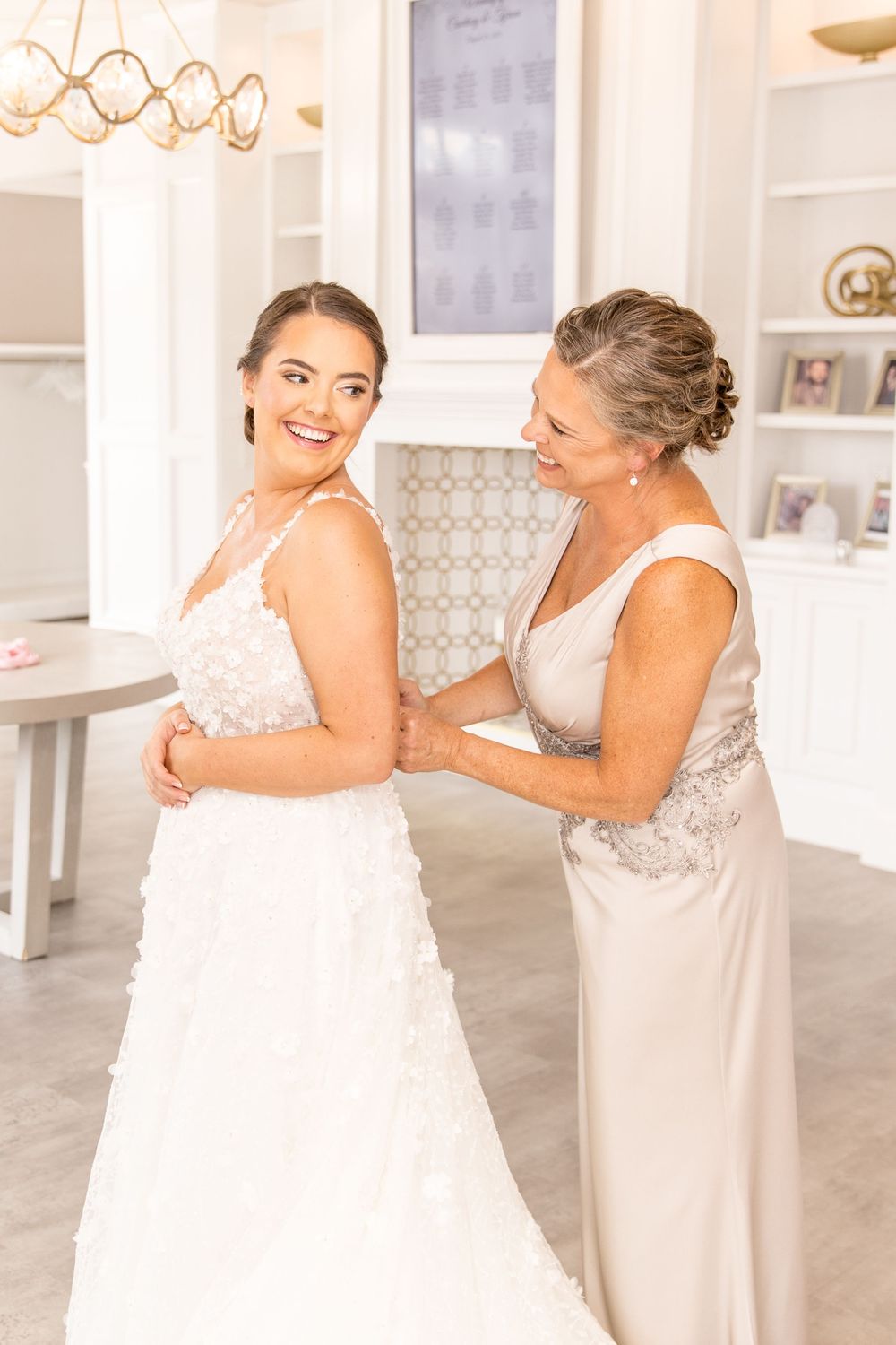 A touching scene unfolds in an elegant white room during a wedding preparation moment.
