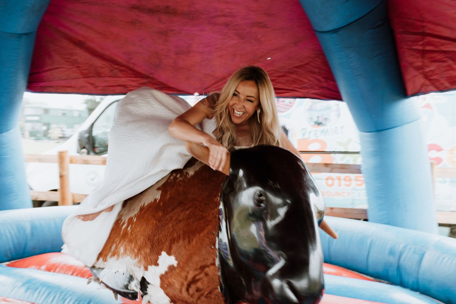 Bride laughs while riding a mechanical bull at wedding reception at Stanford Farm