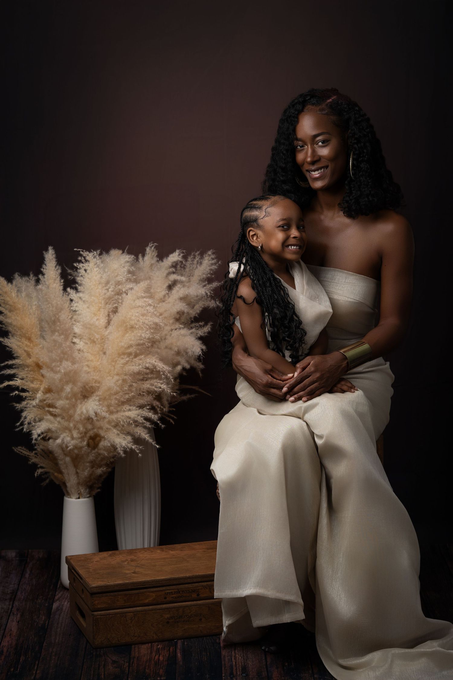 Romantic portrait series featuring two people in ivory gowns with pampas grass bouquet against dark backdrop.