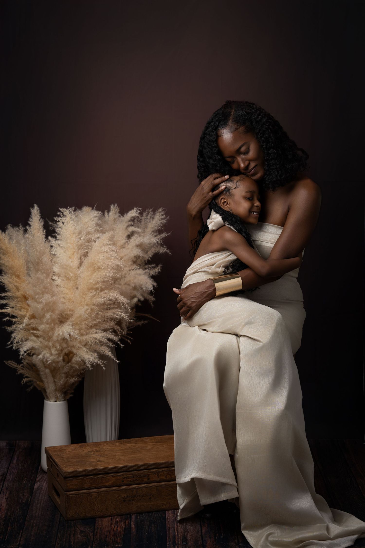 Intimate portrait of maternal love with cream pampas grass decor against dark background in studio setting.