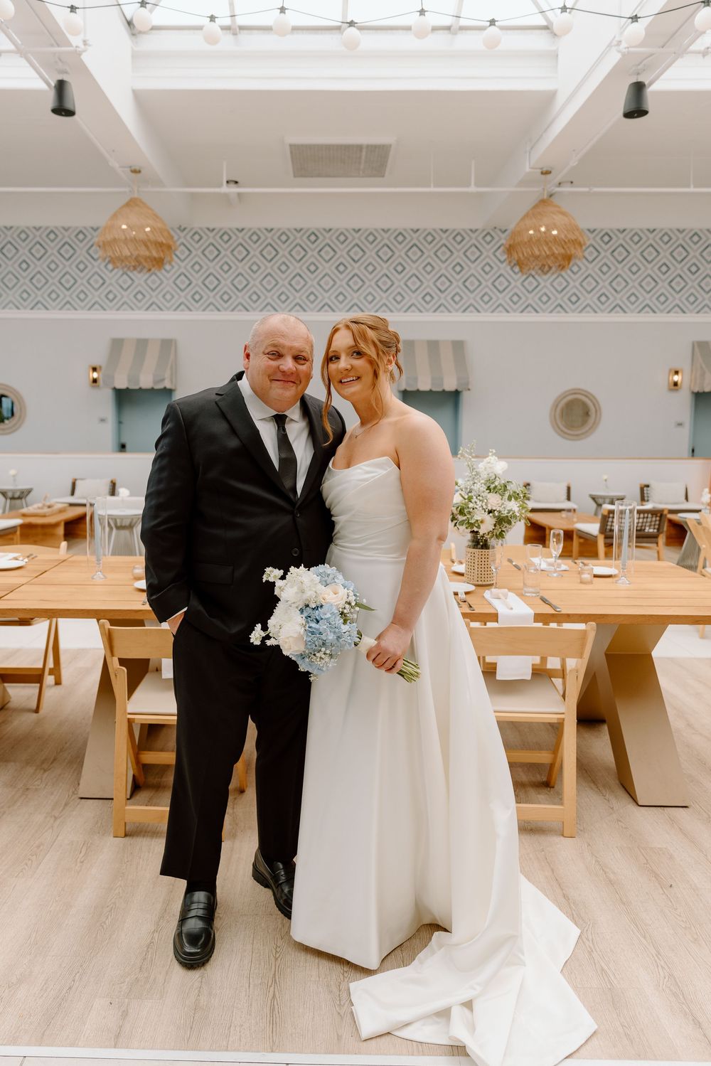 Wedding celebration in modern restaurant with wooden tables and geometric pendant lights in a bright, airy space.