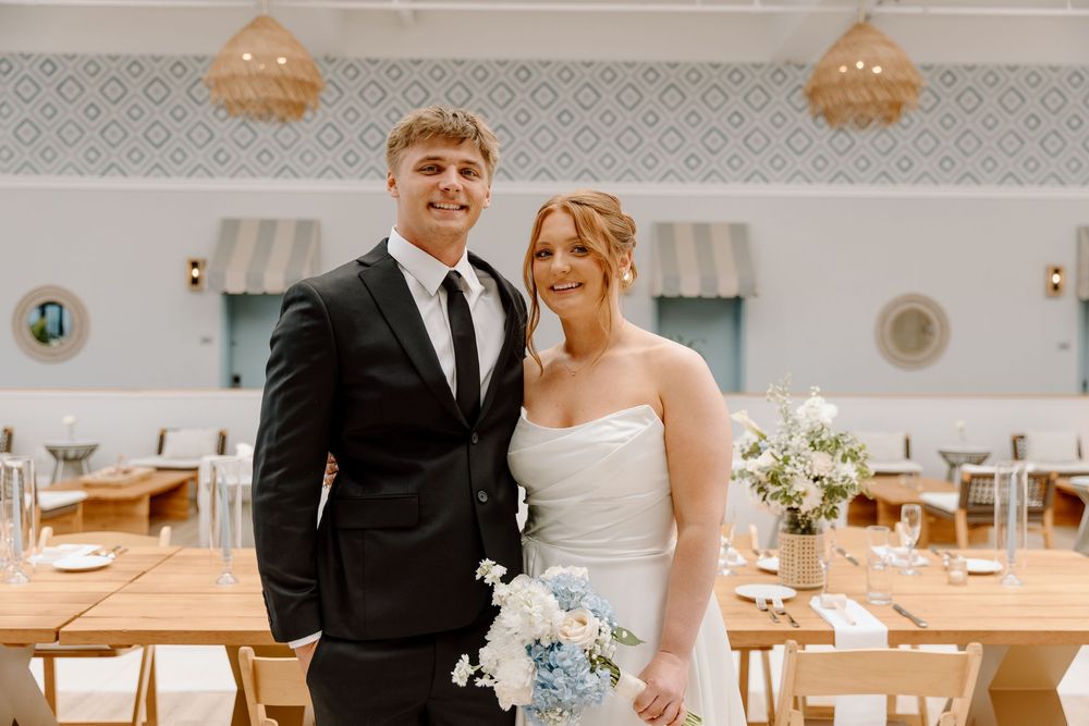 A formal wedding celebration at an elegant venue with light blue floral bouquet and wooden dining tables in the background.