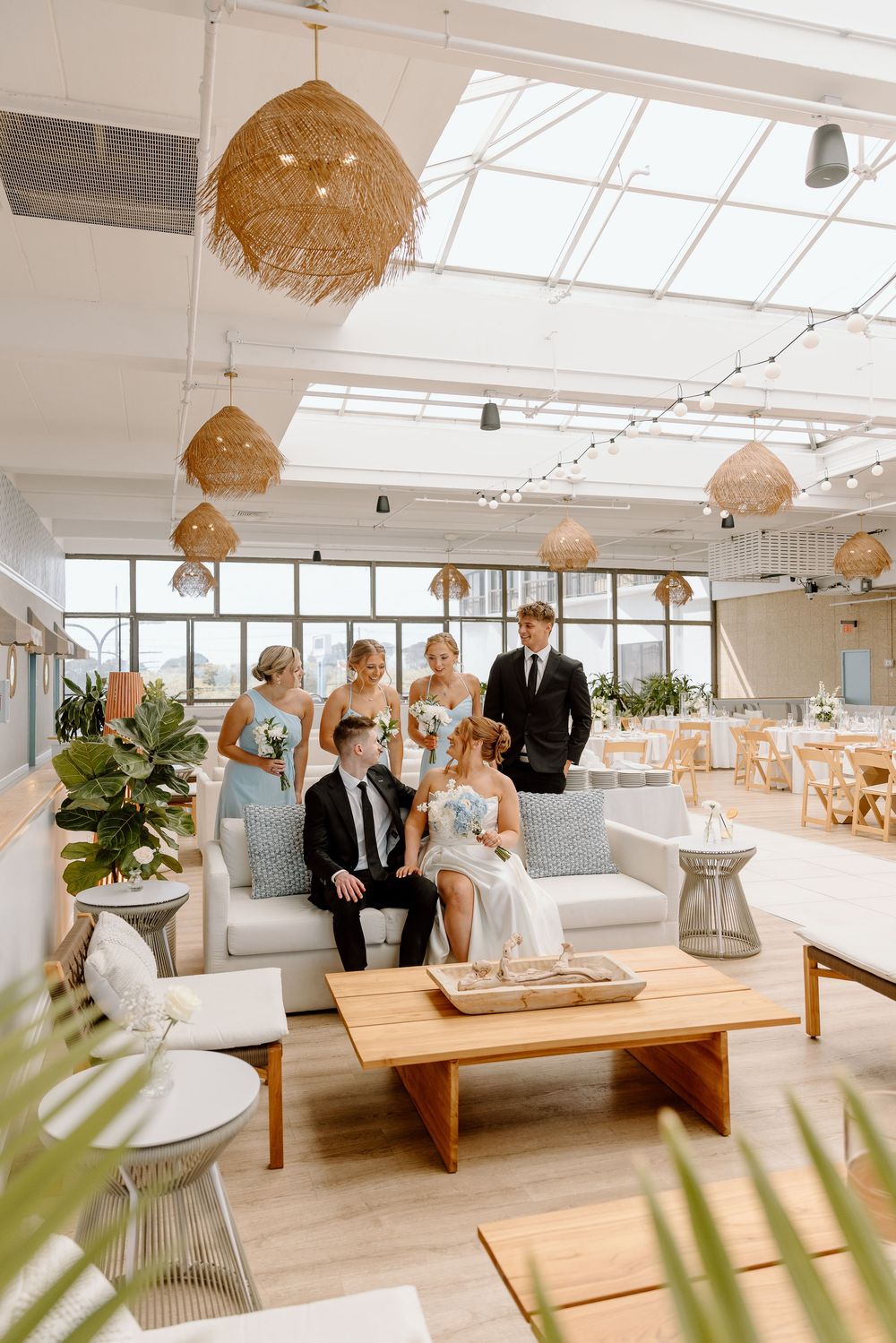 Modern coastal event space with minimalist decor features rattan pendant lights, white walls, and wooden bench seating.