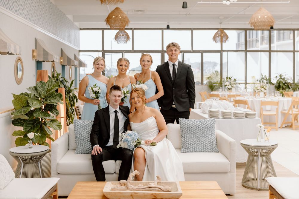 Wedding party relaxes in a modern white sunroom with woven pendant lights and coastal decor.
