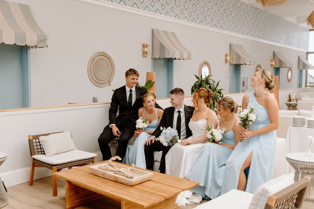 Elegant gathering in a blue and white decorated venue with people in formal attire seated on a white couch.