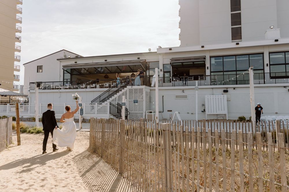 A sandy beach with wooden fence posts extending along the shoreline next to beachfront buildings under a cloudy sky.