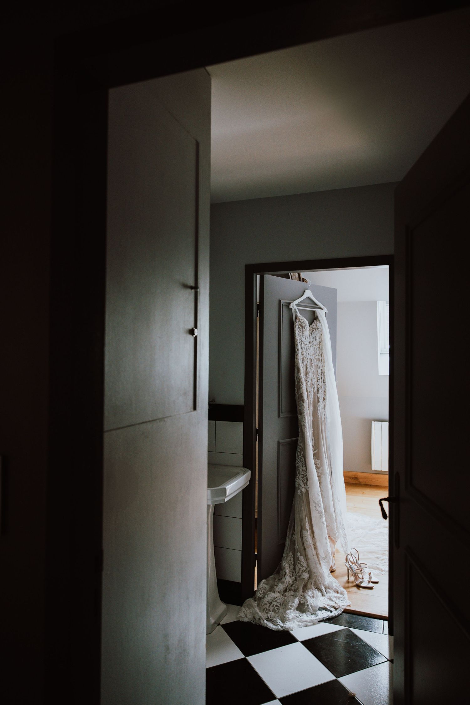A vintage white lace wedding dress hangs in a doorway casting dramatic shadows in natural light.