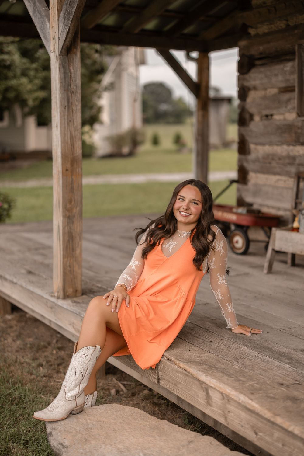 A rustic country porch scene with white cowboy boots and a bright coral dress on a warm summer afternoon.
