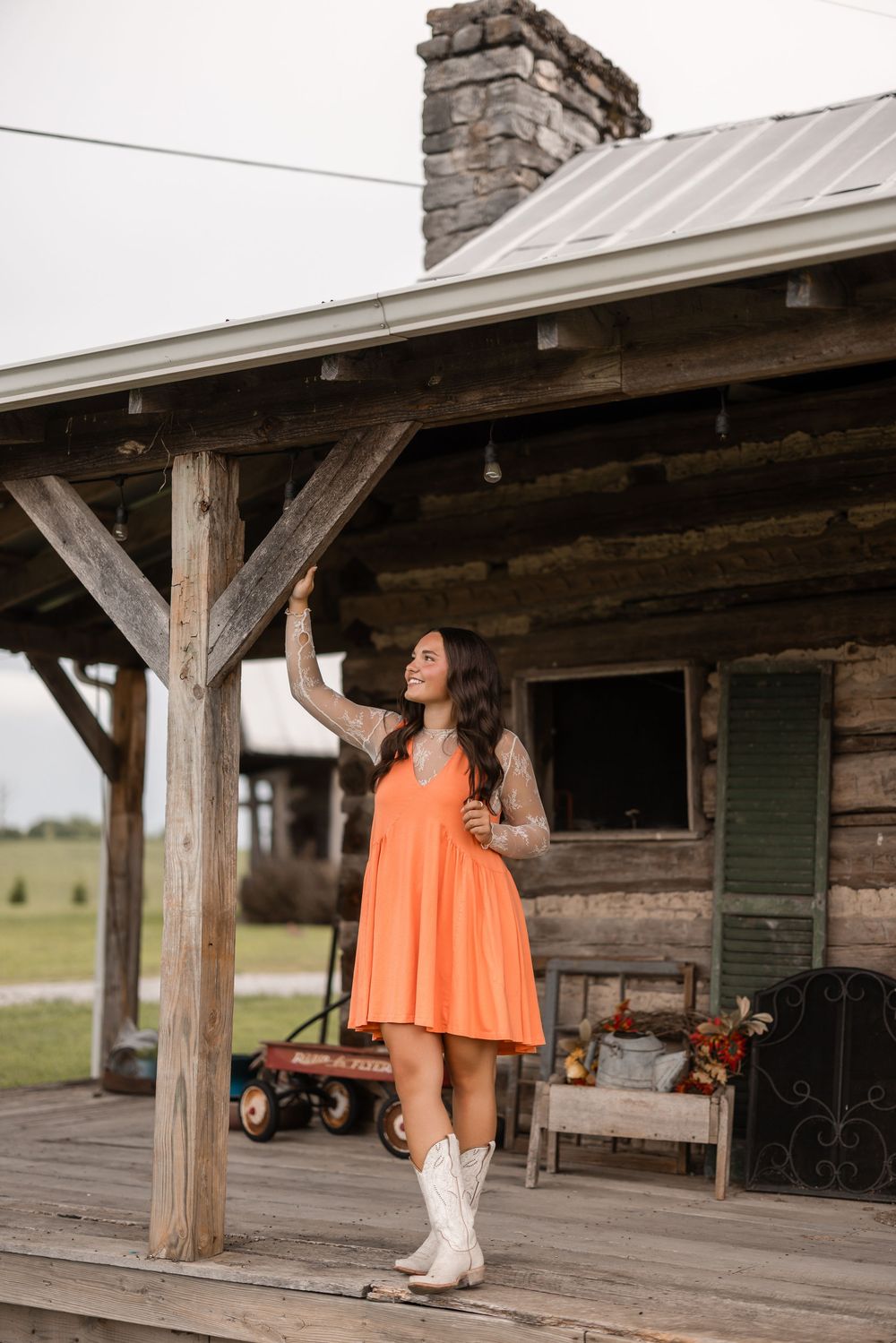 Person in orange top and cowboy boots poses on rustic wooden porch of country cabin.