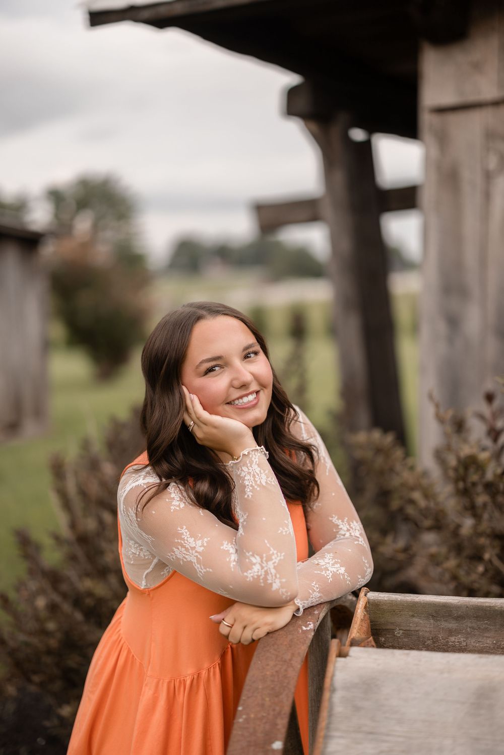 A figure in a flowing orange dress and sheer lace sleeves poses outdoors in a whimsical photoshoot series.
