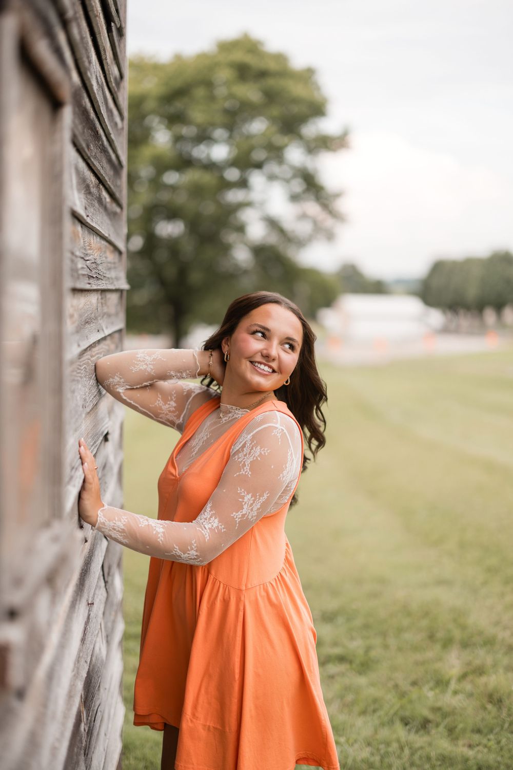 A stylish orange sundress outfit captured in front of a rustic wooden wall on a grassy field.