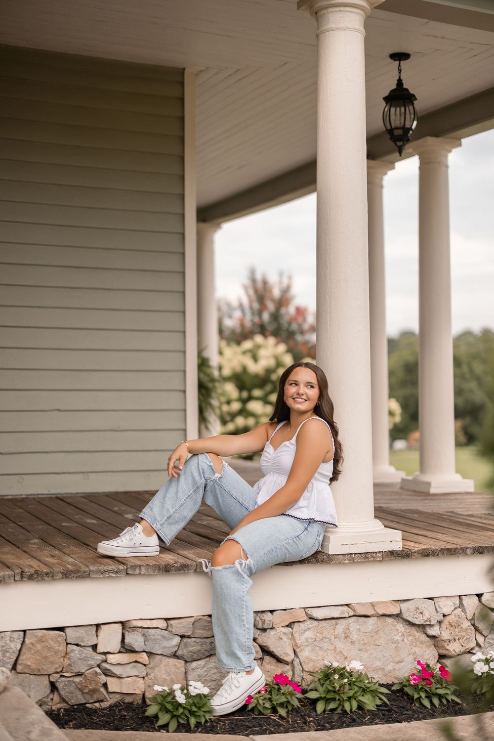 Casual summertime portrait on a rustic stone and wood porch with white columns and colorful flowers below.