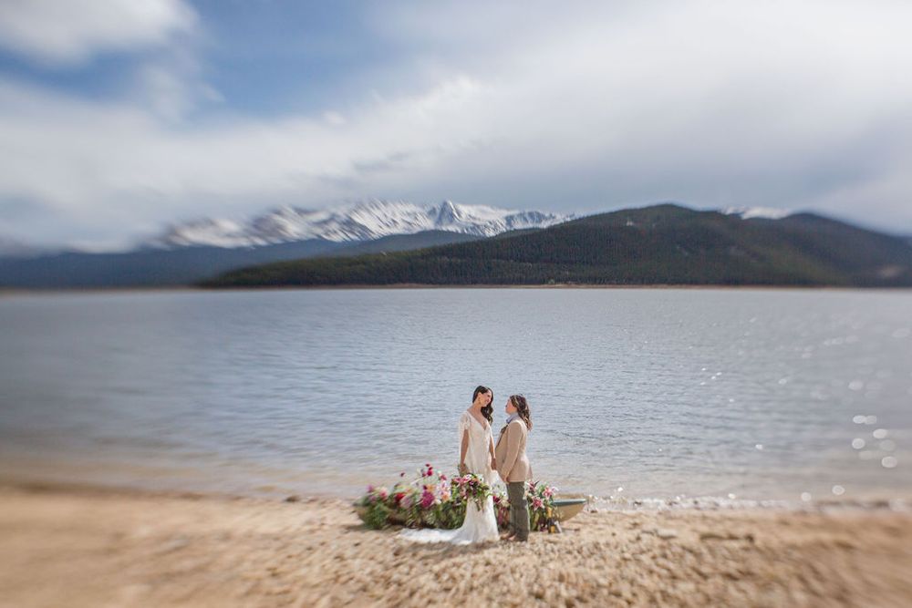 A wedding ceremony scene on a mountain beach with snow-capped peaks in the background.