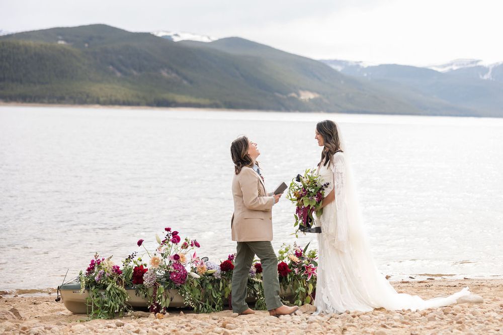 A romantic lakeside proposal scene with flowers decorating the shore and mountains in the background.