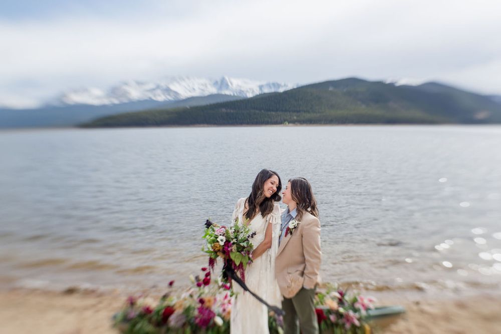 A couple shares an intimate moment during their lakeside wedding with mountains in the distance.