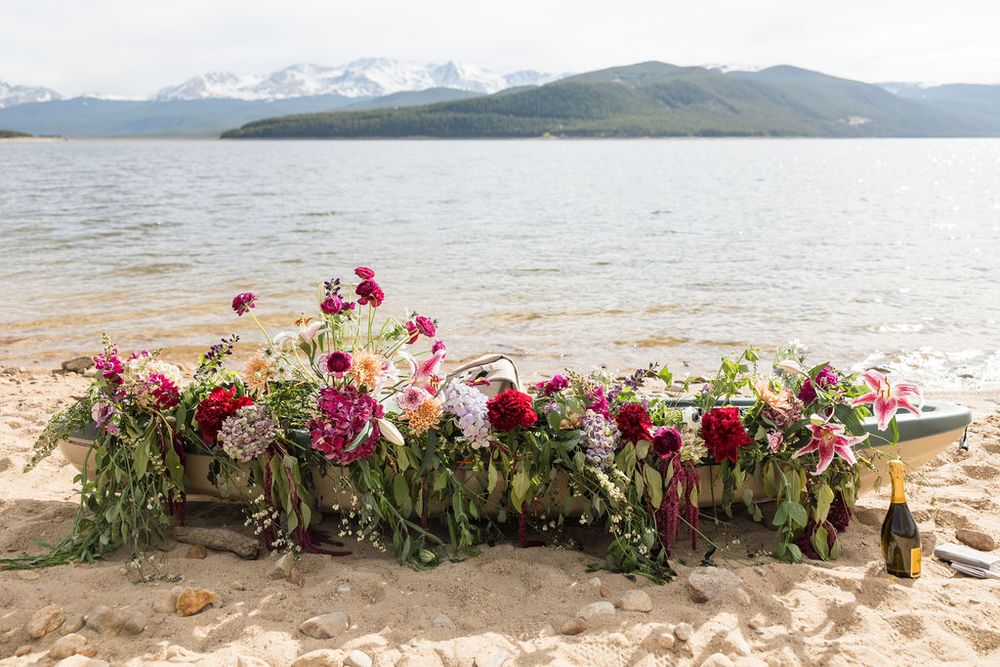 Red and pink floral arrangements line a sandy beach with mountain views in the background.