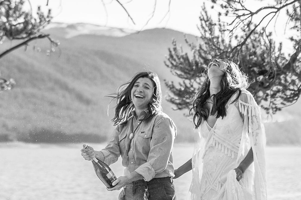Two people sharing joyful laughter while celebrating outdoors on a sunny mountainside.
