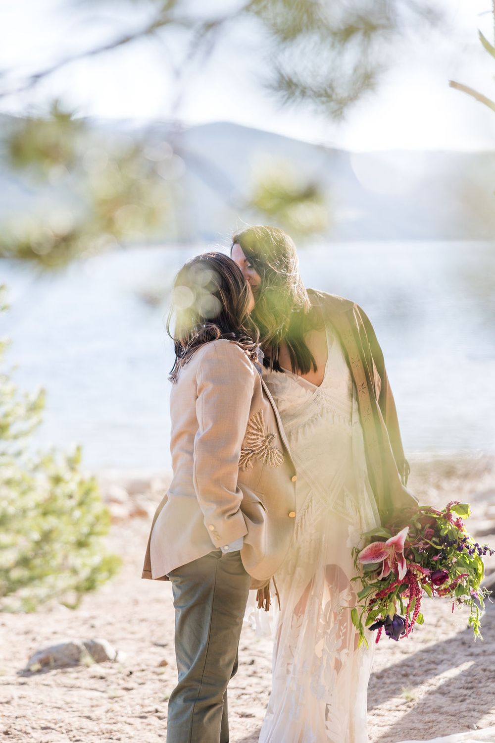A romantic mountain elopement photo showing a loving couple embracing with a bouquet against a dreamy blurred background.