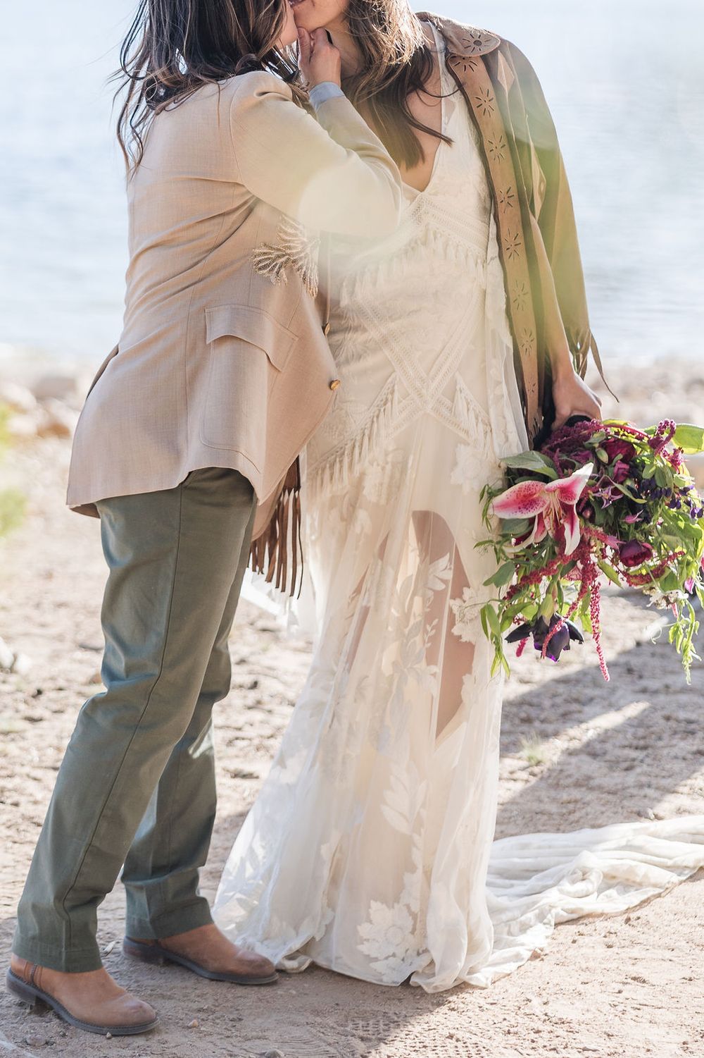 Close-up photo showing brown cowboy boots next to a cream colored wedding dress skirt in a desert setting.