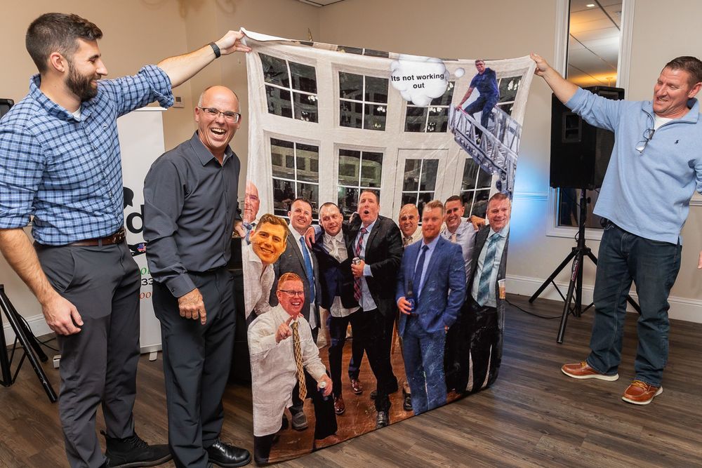 Party guests holding up and viewing a large photo print during an indoor celebration.