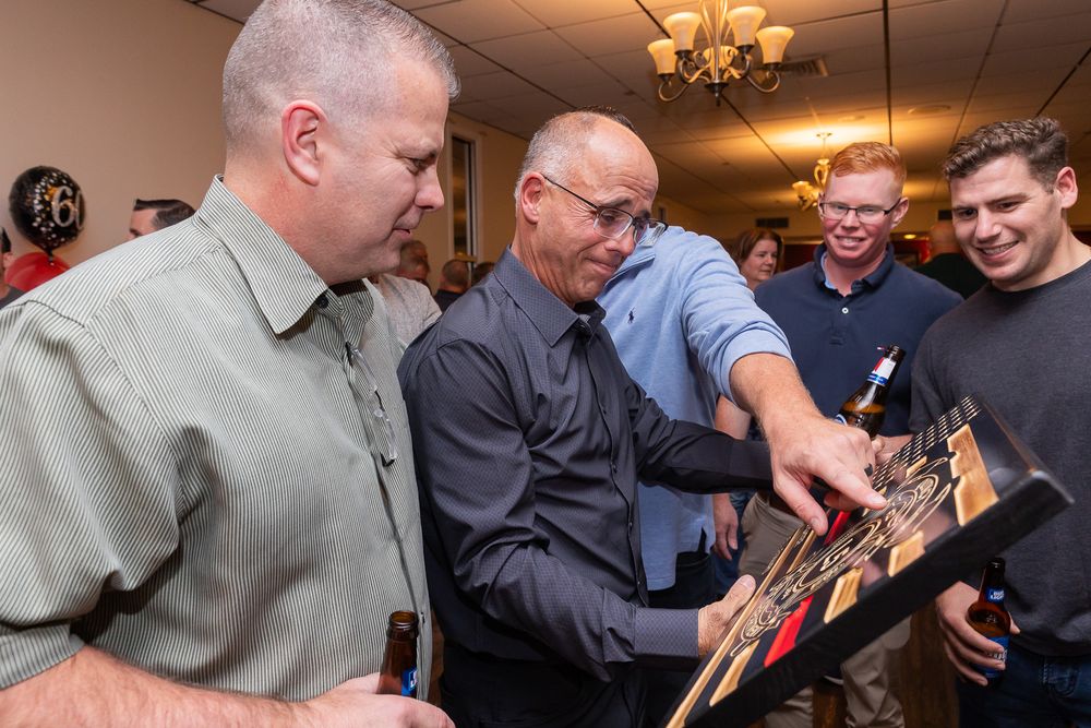 A group looks closely at a wooden plaque or frame together in an indoor setting.