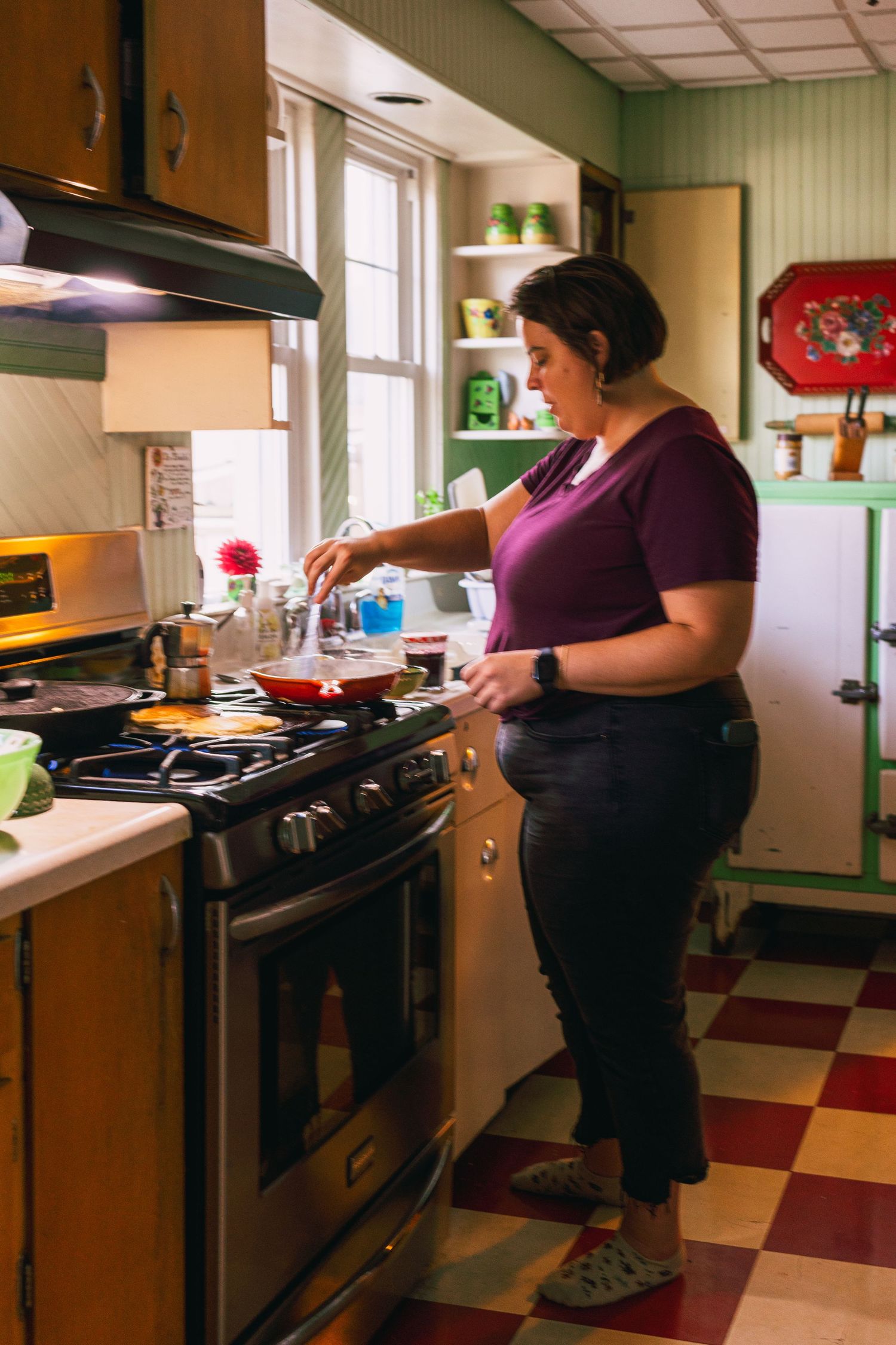 Someone cooking at the stove in a retro kitchen with checkered floors and green walls.