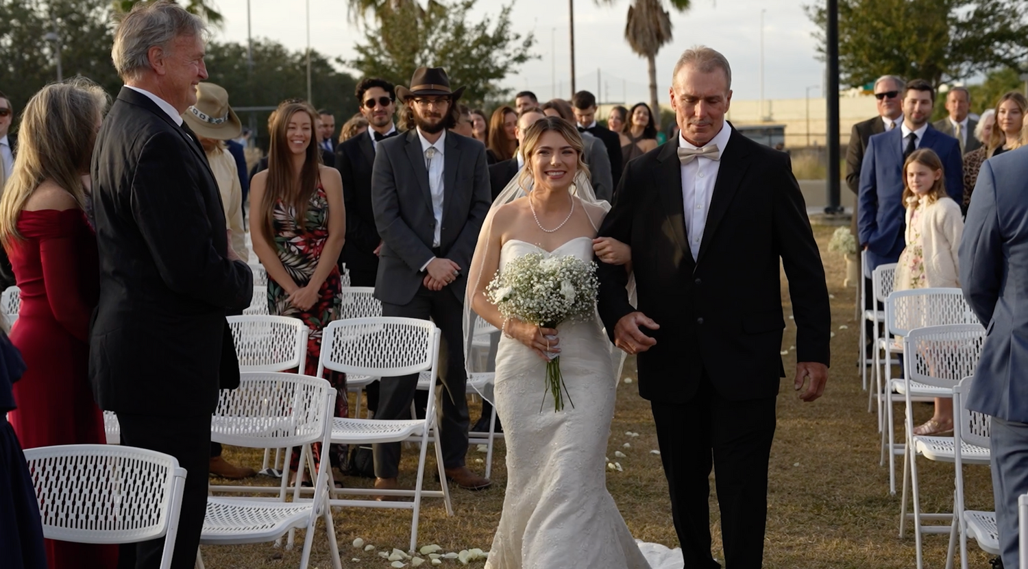 An outdoor wedding ceremony setup with white folding chairs on a lawn during a sunny day.