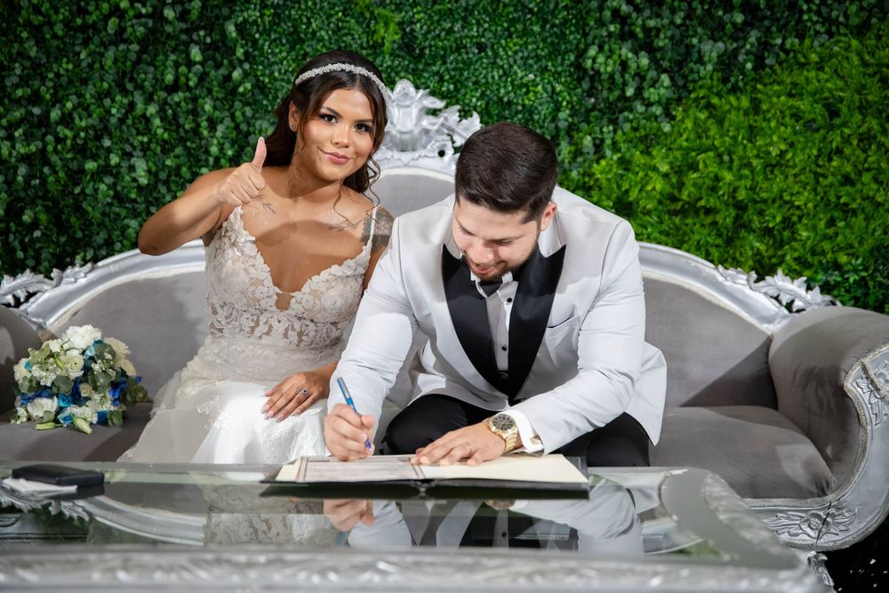 Wedding couple signs documents at elegant green hedge wall backdrop.